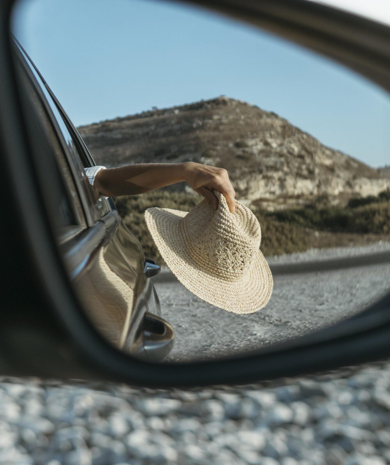 mujer-sosteniendo-el-sombrero-por-la-ventana-en-la-vista-del-espejo-de-coche mujer-sosteniendo-el-sombrero-por-la-ventana-en-la-vista-del-espejo-de-coche